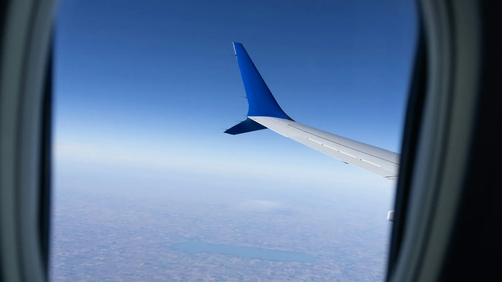 An aeroplane wing seen through a cabin window above the clouds